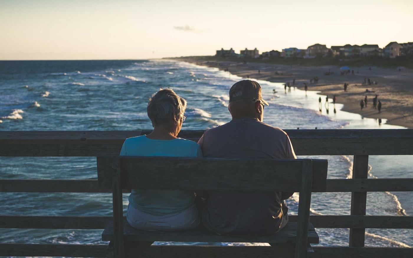 Married couple a bench staring at ocean.